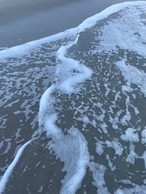 The view of a wave as it moves up the sandy beach. The tip of the wave is bubbly with random bubbles scattered about the rest of the picture as other waves meet the sand and pull away from it.