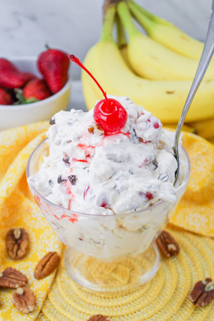 Fluff in a clear glass bowl with spoon and cherry on top.