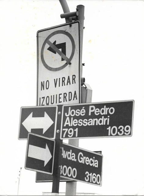 A fotografia em preto e branco mostra uma placa de trânsito da cidade de Santiago na qual está escrito: “Não virar à esquerda". Além desta há outras duas placas com nomes de ruas da capital chilena.