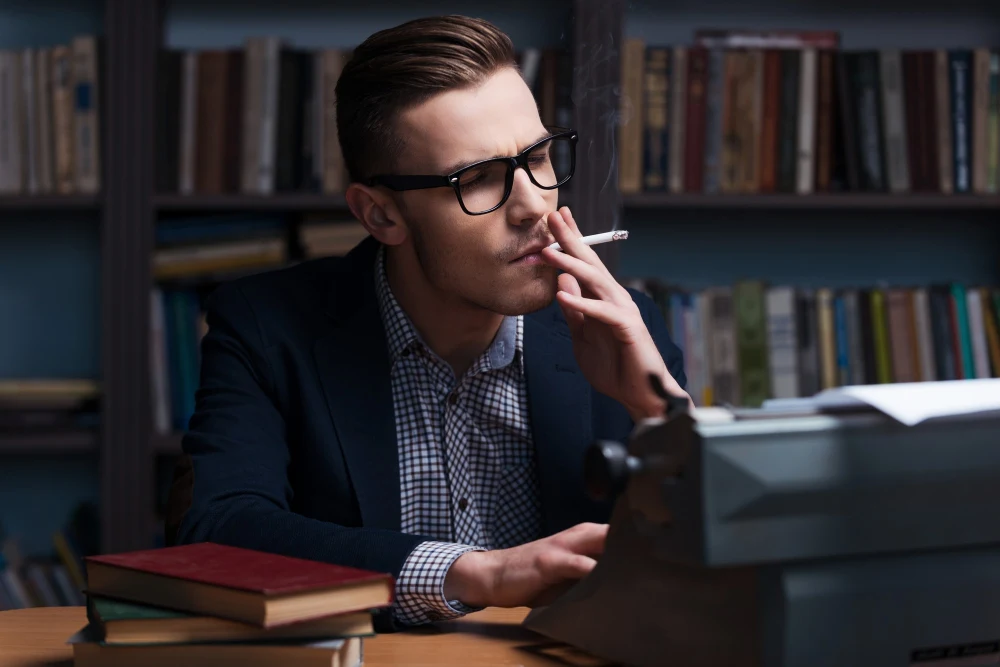 Mężczyzna pali papierosa na tle biblioteczki wypełnionej książkami