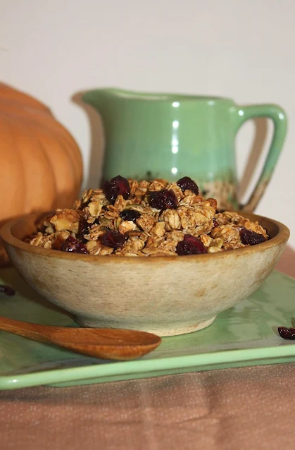 Bowl of pumpkin spice granola with spoon and pitcher of milk.