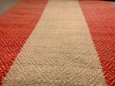 An angled close-up of handwoven fabric with wide pink and white stripes, highlighting the diamond pattern woven into it.
