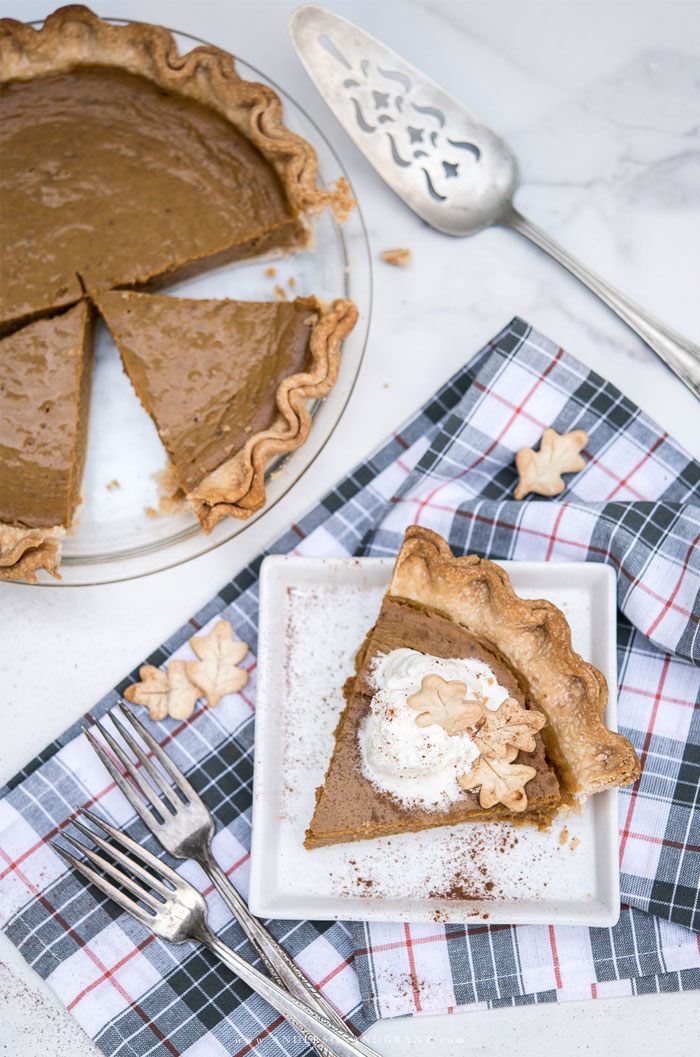 Pumpkin pie with one slice on a white plate