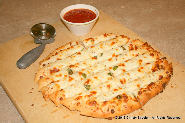 The cheesy pizza is sliced and served on the large cutting board.  A side of extra sauce is served for dipping.