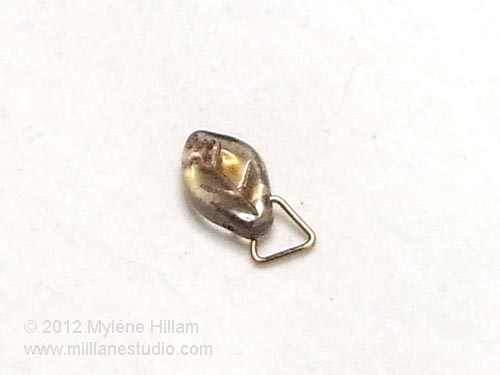 Triangle jump ring with one prong inserted into a leaf bead.