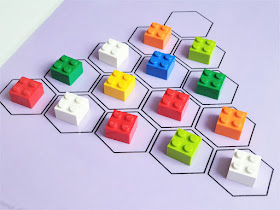 na zdjęciu plansza do gry w trójkątną wersję samotnika. Plansza jest w kolorze fioletowym z piętnastoma polami ułożonymi w kształt trójkąta, na czternastu polach leżą kolorowe klocki lego, jedno pole na wierzchołku planszy jest puste