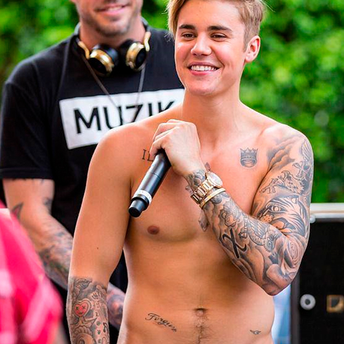 Justin Bieber sem camisa sorrindo com o microfone na mão