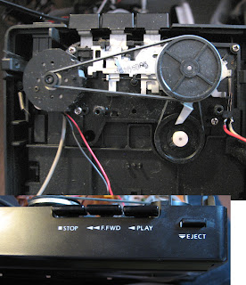 [Image: The cassette player opened, showing the tape drive mechanism with several wheels connected to each other via rubber strings, and the control buttons connected to them via springs and levers.]