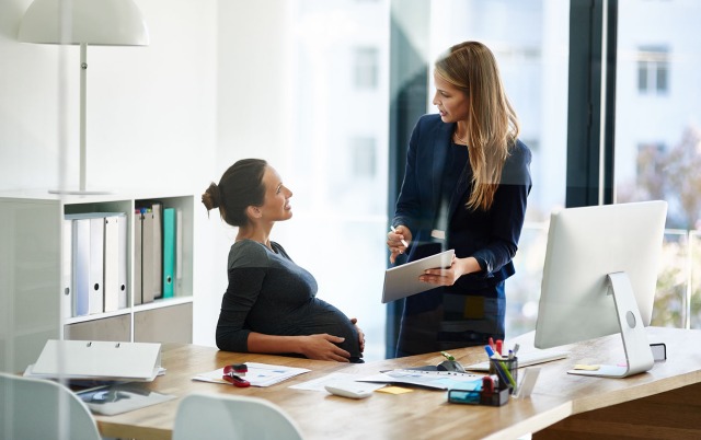 Pregnant woman at a desk talking to a coworker