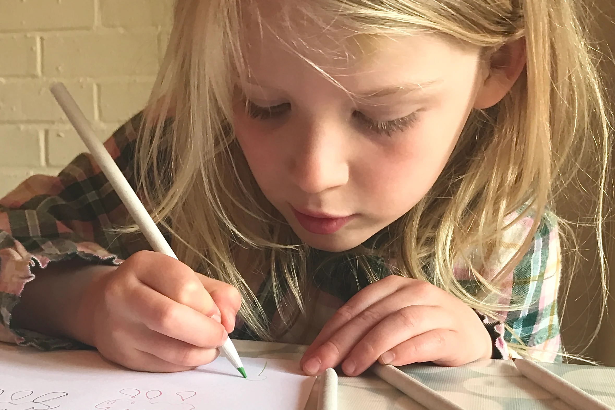 A 5 year old girl writing with a pencil at a desk