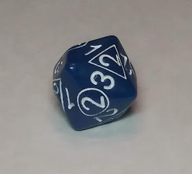 An oddly-shaped chunk of blue plastic. It has a variety of numbers between 1 and 4 printed on it in white, some of those numbers in a circle or a triangle. The die is shaped such that whenever it lands, a number with no shape will land on top, and beside that number is one number in a circle, and one number in a triangle.