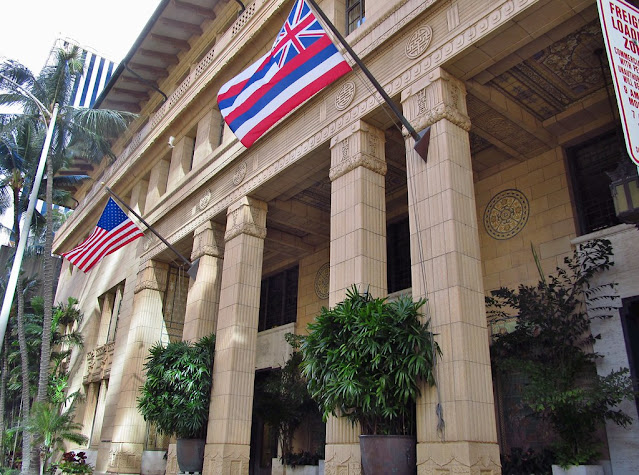 Exterior of a beige building with columns, with American and Hawaii flags. The Alexander and Baldwin Building in Honolulu.