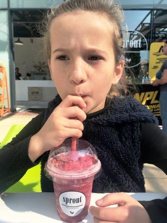 Frowning girl (because of sun) drinking a Sprout berry smoothie