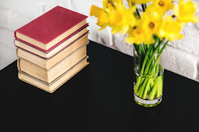 A pile of books and a vase of daffodils on a black table.
