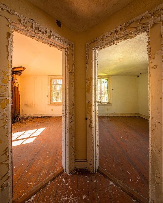 An image of two identical doorless door frames on either side of landing, looking into two rooms which both have windows, and the right one has a reflection of the sun through another window. Taken by Walter Arnold.