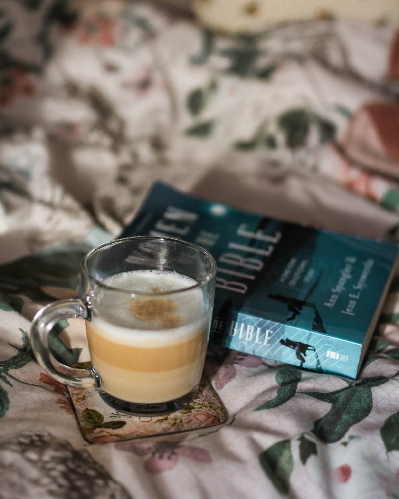 latte in glass mug and blue devotional book sitting on floral betting