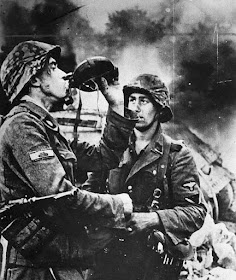 Two Waffen SS soldiers have a drink. In the background burns a T-34 tank