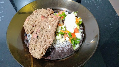 Em cima da mesa, prato com feijão, arroz, salada e duas fatias de bolo de carne