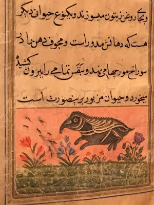 A page from a yellowed Arabic manuscript, with four lines of text in black above a pink panel with a grey and tan anteater frolicking through a field of bright coral, blue, and purple flowers over rolling green grass.