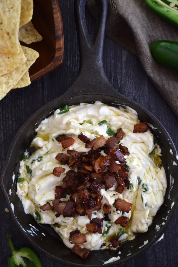 Cooked, diced bacon being added back into the skillet with creamy cream cheese and flavorful jalapenos for a delectable Jalapeno Popper Dip.