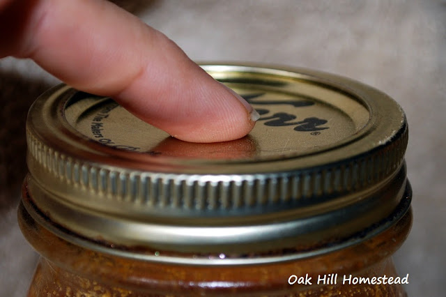 A woman's finger gently testing the canning lid to see if it has sealed correctly.