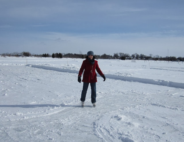 A woman wearing a red coat and ice skates stands on a frozen lake