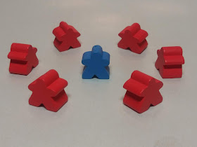 a circle of six red meeples surrounding a blue meeple, to symbolise the divisive nature of some people