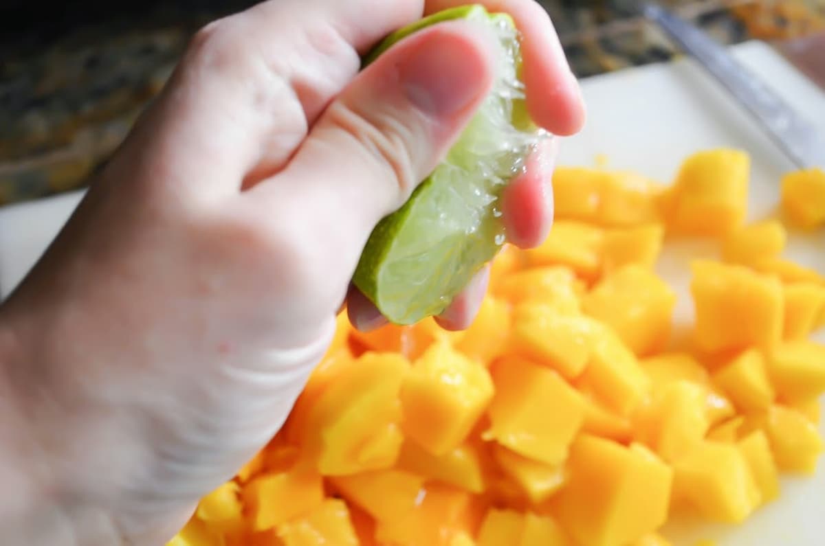 Lime being squeezed over diced mango on a cutting board.