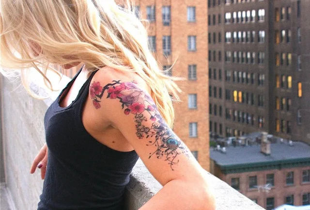 Chica rubia en la azotea de un edificio de New York, apoyada en la cornisa vemos su tatuaje de flores en un brazo