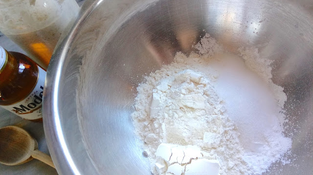 a large stainless steel bowl filled with dry ingredients for Sourdough Beer Bread sitting next to a bottle of beer and a jar of sourdough starter