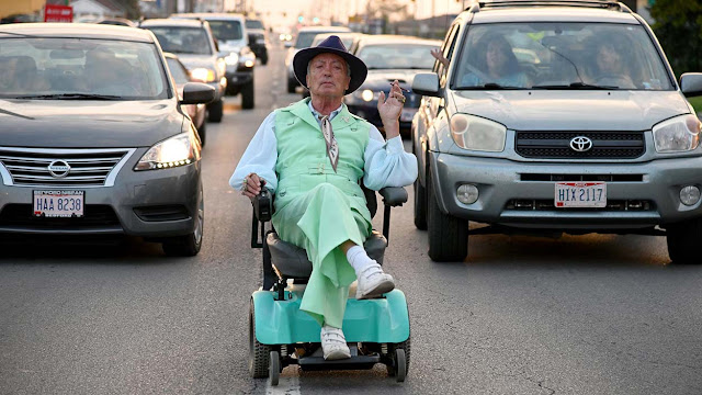 Udo Kier riding a rascal down the street