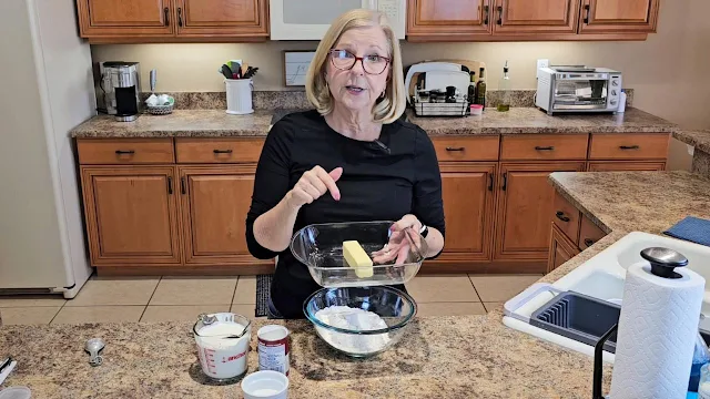 A woman in a kitchen holding a glass baking dish with a stick of butter in it.