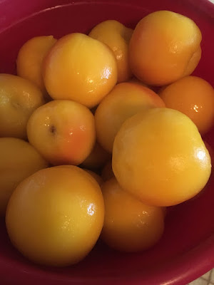 A pile of skinned gold-pink peaches in a red bowl. They look slimy and syrupy.