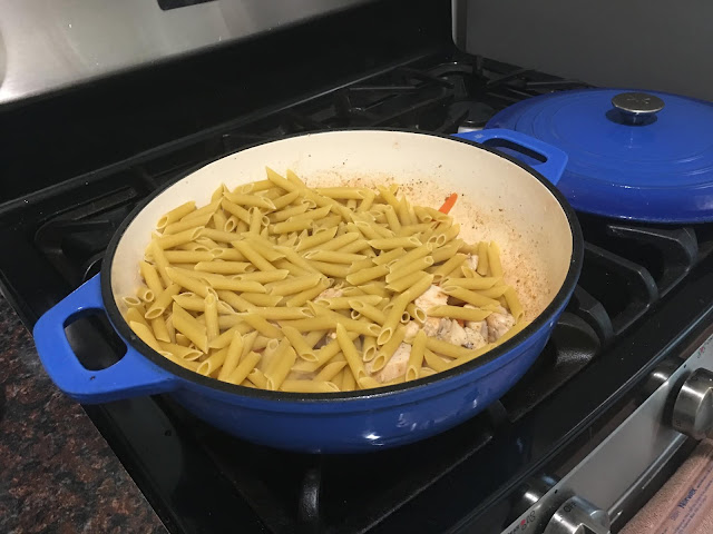 The uncooked pasta in the pan with the chicken and carrots. 