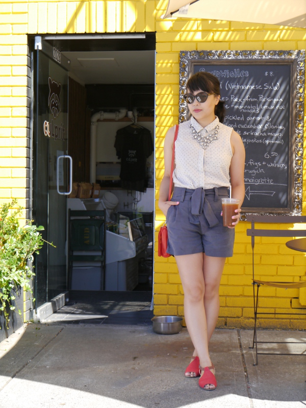Vancouver fashion blogger Lisa Wong stands in front of a local coffee shop wearing a JACHS sleeveless blouse, Cici tie-waist shorts from Two of Hearts Boutique, a sparkly J. Crew statement necklace, Ray Ban cat-eye shades, a Roots bag, and Rachel Comey x Urban Outfitters sandals.