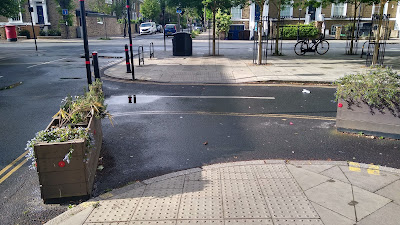 A view across the side street with planters either side of a dropped kerb crossing point.