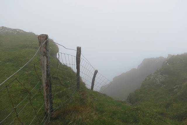 A wire fence trails off and ends suspended over the edge of steep cliffs.