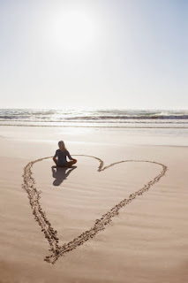 Heart drawn in sand around a woman meditating.