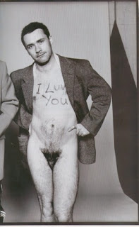 damien hirst, naked except for a suit jacket, with his dick tucked between his legs and I luv you written on his chest
