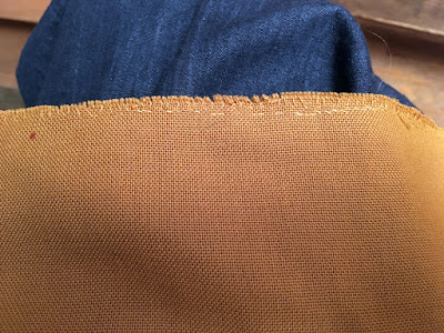 Mustard-brown fabric with a very frayed seam allowance and two shades of bright-yellow thread at the seam.