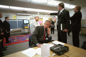 Color photo of Deputy Assistant Dan Bartlett pointing to news footage of the World Trade Center, President George W. Bush gathers information about the attack Tuesday, Sept. 11, 2001, from a classroom at Emma E. Booker Elementary School in Sarasota, Fla