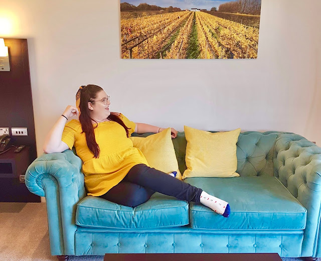 Plus size travel and lifestyle blogger The Owlet sat on a blue sofa in a hotel room in South Wales