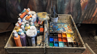 A well used artist pallet and paints, in a suitcase.