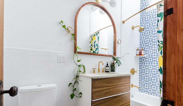 Small bathroom with white walls and blue tile with plants on the corners of the vanity.