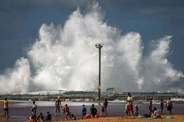 Families sit on North Narrabeen Beach as waves crash into a rock pool in Sydney on April 18, 2025, as large swells strike Australia’s east coast. Photo by David Gray/AFP