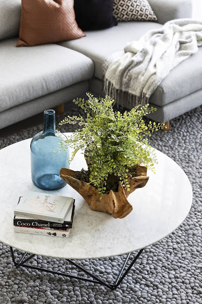 Sala de estar moderna y lujosa con mesa de centro de mármol, planta falsa y jarrón de vidrio azul de West Elm