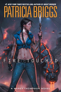 Cover image description: Mercy Thompson wears a blue tank top and jeans while holding a spear. Behind her there's a menacing-looking dog made out of cooling lava.