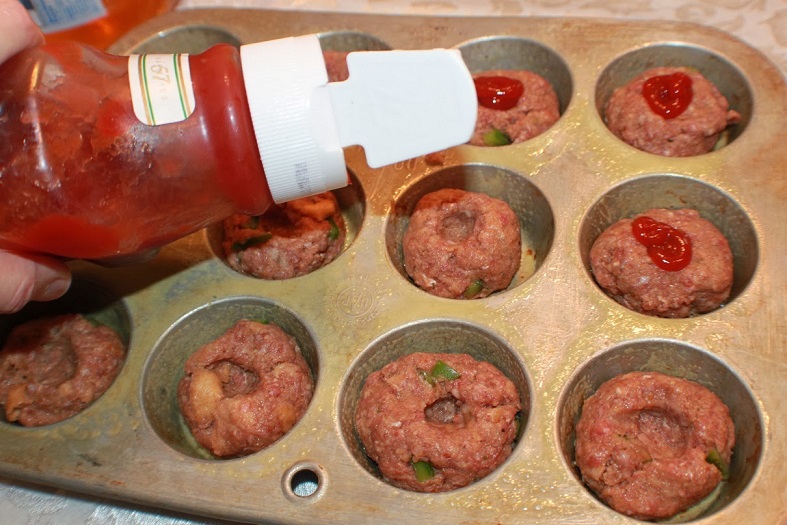 these are miniature  raw meatloaves made in a cupcake tin for individual servings. These are on a white plate with ketchup and baked green peppers on top