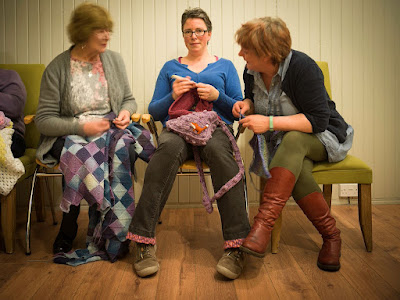 a group of 3 women, sitting with knitting/ crochet engaged in converstaion