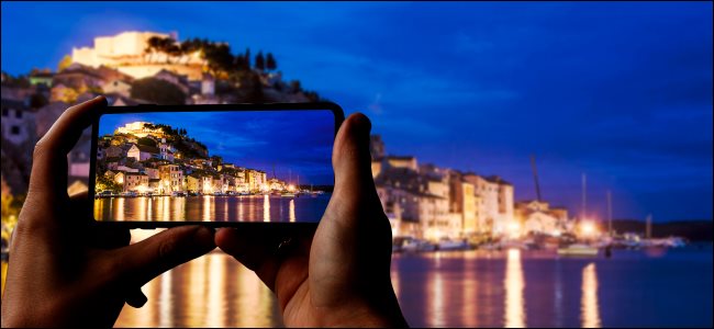 هاتف ذكي يلتقط صورة لمدينة وبحر ليلاً.